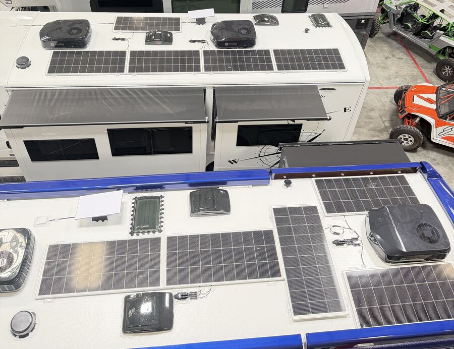 Motorhomes parked in rows inside the 24/7 MotorCoach shop, seen from above, with solar panels mounted on their roofs alongside rooftop air conditioners, vents, and retracted awnings.